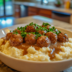 A bowl of mashed potatoes topped with frozen meatballs in rich brown gravy, garnished with fresh parsley. ( Frozen meatballs and gravy recipe )