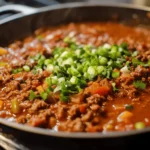 A steaming pot of Meat Church chili recipe with ground beef, tomatoes, and colorful bell peppers, garnished with chopped green onions and cilantro.