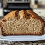 Moist banana bread recipe with oil : A freshly baked moist banana bread loaf, sliced open to reveal its soft and fluffy texture, sitting on a white plate in a home kitchen.